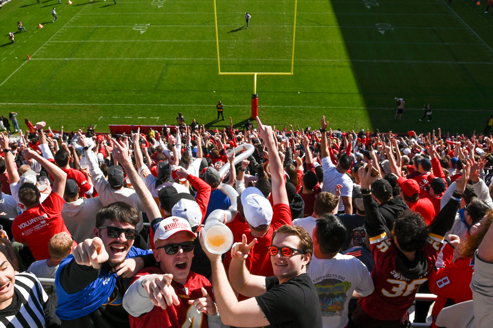 Crowd at a DC Defenders game drinking beer from a snake like tube