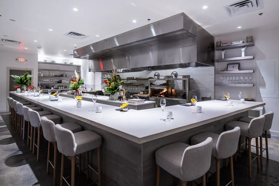 A modern, bright kitchen with a large U-shaped counter surrounded by barstools, featuring fresh flowers and elegant place settings.