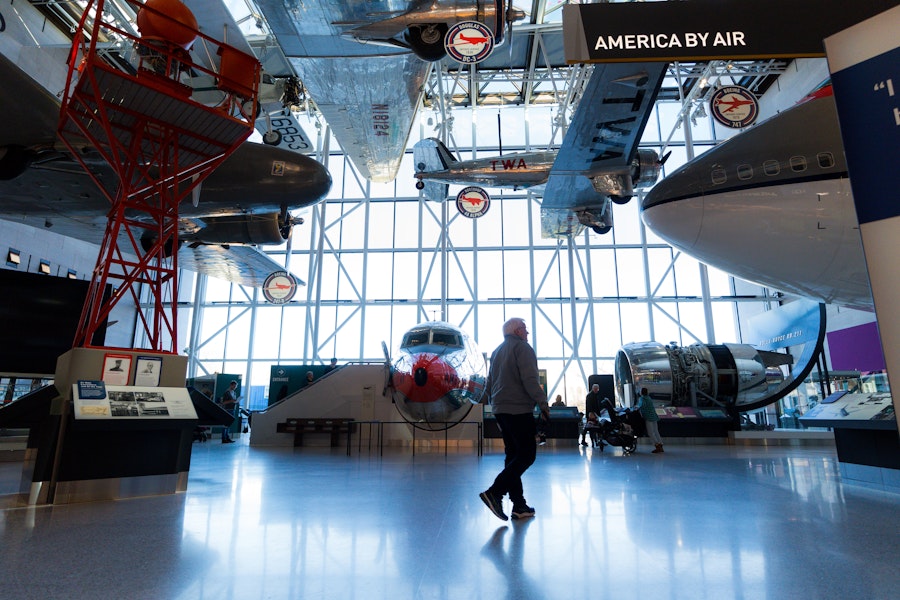 A visitor walks through the "America by Air" exhibit at the National Air and Space Museum, surrounded by historic airplanes displayed from floor to ceiling.