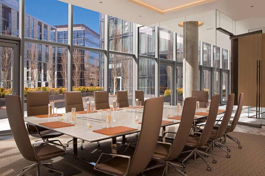  A sleek, modern boardroom at the Conrad with floor-to-ceiling windows offering a view of the city, featuring a large table surrounded by high-backed executive chairs in a bright, professional setting.