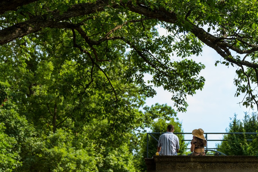 Two people sit together on a stone wall under the shade of large trees in Meridian Hill Park.