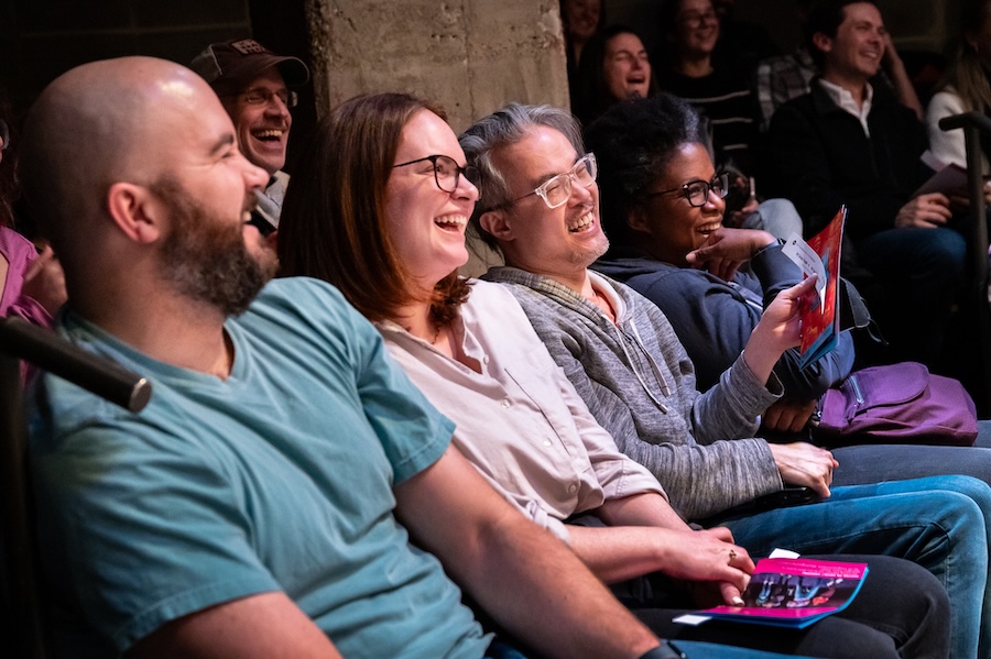 A group of people in the audience laughing and enjoying a live comedy or theater performance.