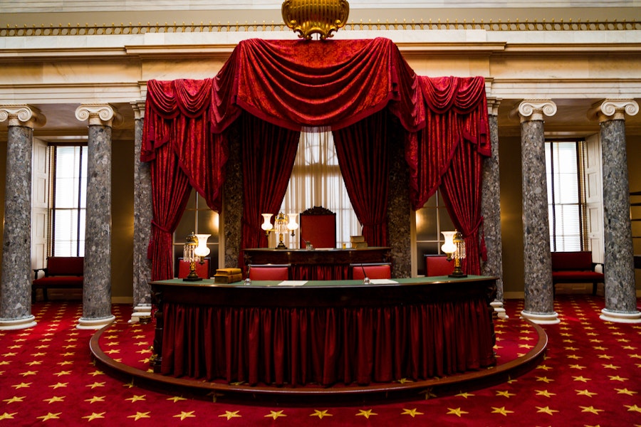 The richly decorated Old Senate Chamber in the U.S. Capitol, with red draped curtains, marble columns and gold accents.