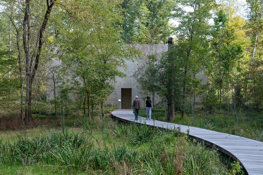 Visitors walk along a curved boardwalk toward the concrete building that houses Richard Serra’s “Four Rounds: Equal Weight, Unequal Measure.”