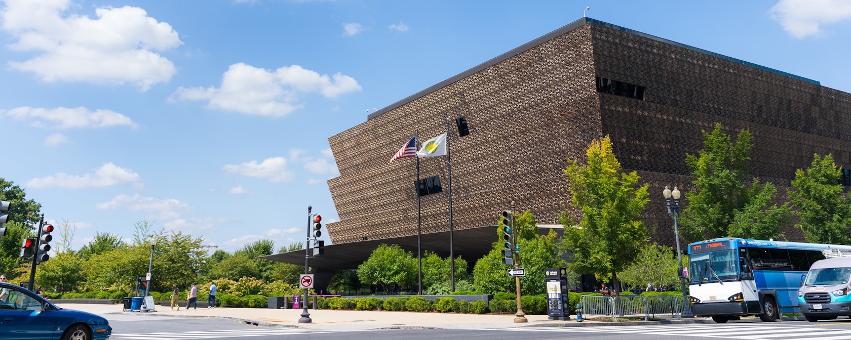 A view of the National Museum of African American History and Culture on a sunny day as cars pass by. . 