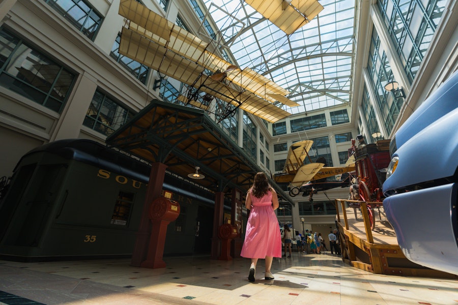 A visitor walks through the National Postal Museum’s grand hall beneath suspended vintage aircraft and a glass ceiling.