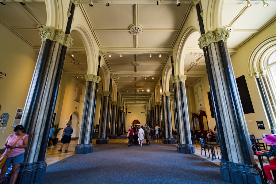 Visitors explore the Smithsonian Castle’s East Wing, lined with tall marbleized columns and arched ceilings.