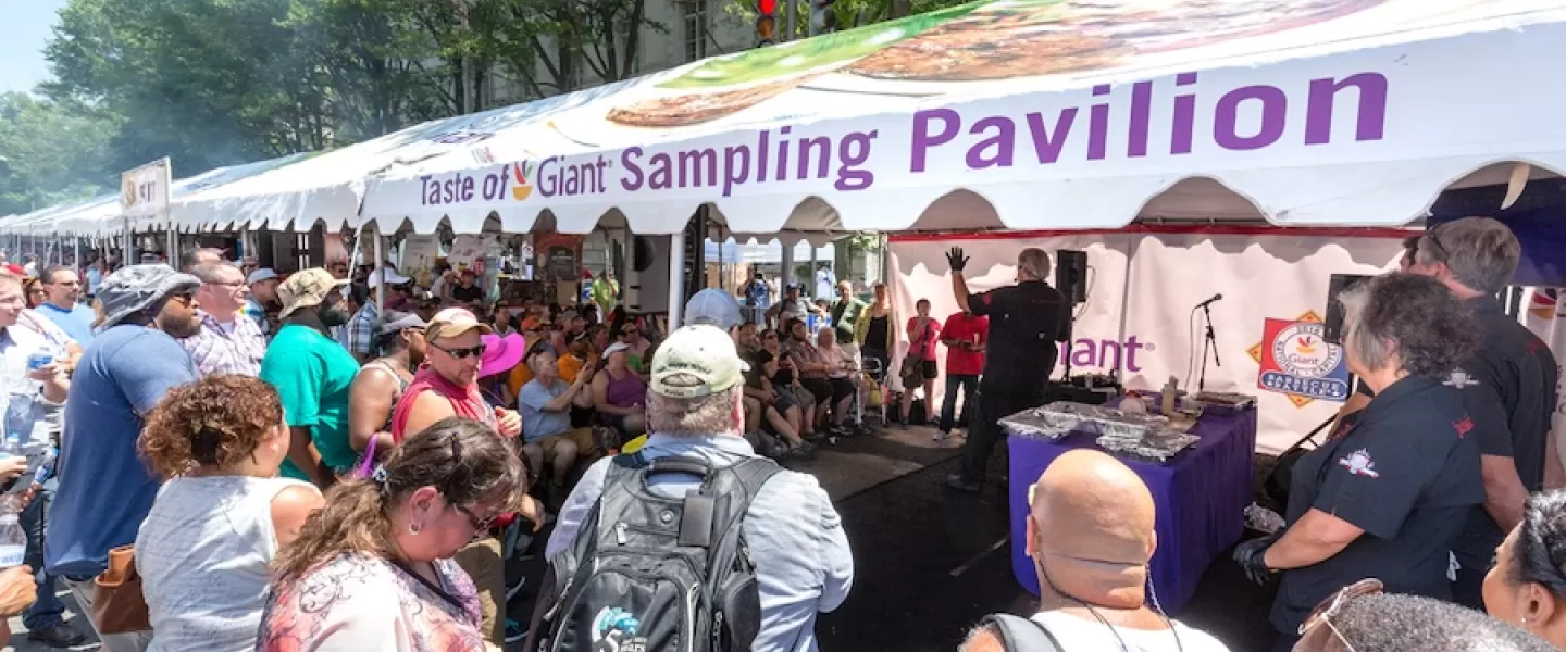 Sampling Pavilion: A large crowd gathered around a sampling pavilion at the Giant BBQ Battle, watching a cooking demonstration under a white tent.