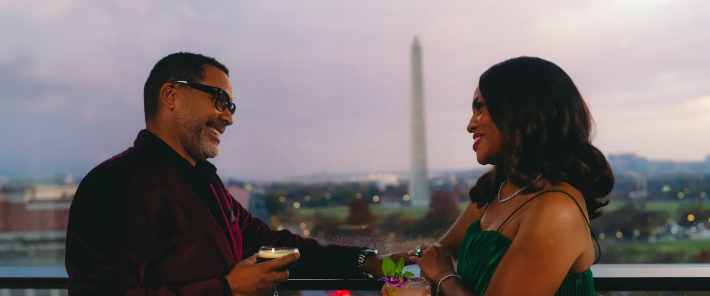 A smiling couple chats over drinks at a rooftop in Washington, DC. 