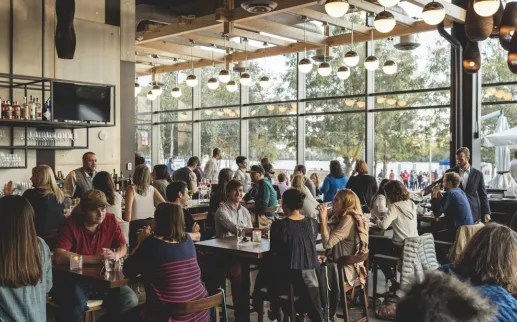 Interior scene of people dining and drinking at District Winery, with the river in the background. 