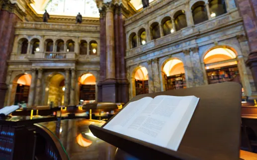 An open book rests on a lectern inside the ornate reading room of the Library of Congress.
