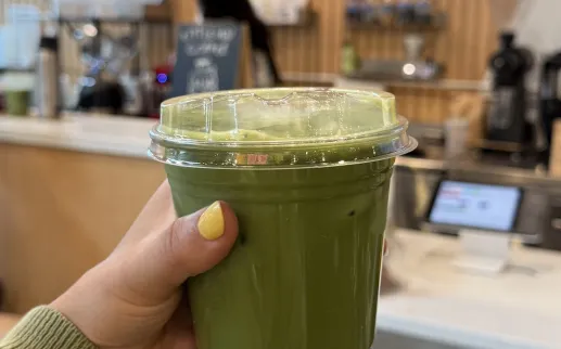 A hand holds up a matcha drink.